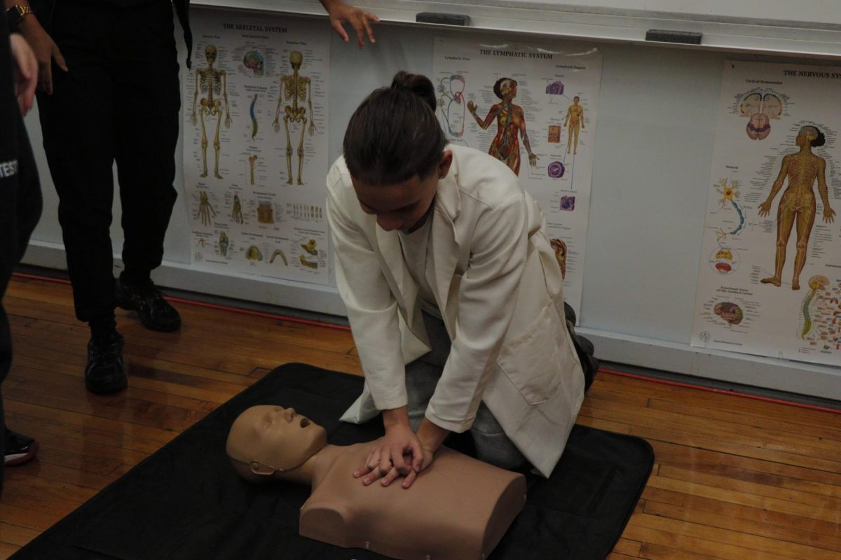 A health student demonstrates how to perform CPR on a manikin.